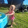 toddler, child, swimsuit, pink, water_table, grass, backyard, sunny, blue_sky, fence, house, barefoot, happy, smiling, outdoor, summer, play, young_child, daytime, nature