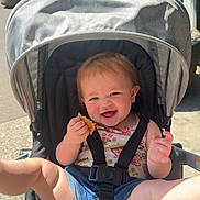 Evangeline joined the competition — help win amazing prizes! baby, child, stroller, smiling, outdoor, sunlight, snack, happy, legs, denim_shorts, floral_top, seatbelt, playful, greenery, daylight, person, infant, cute, summer, nature
