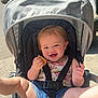 baby, child, stroller, smiling, outdoor, sunlight, snack, happy, legs, denim_shorts, floral_top, seatbelt, playful, greenery, daylight, person, infant, cute, summer, nature