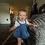 Evangeline is registered to the contest to win money with this photo: toddler, child, smile, blue_dress, socks, living_room, couch, floor, kitchen, door, toy, person, furniture, indoor, happy, blond_hair, face, walking, home, cozy