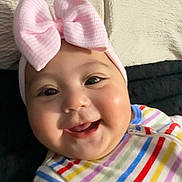 Meghan is registered to the contest to win money with this photo: baby, infant, child, bow_headband, pink_bow, smile, chubby_cheeks, onesie, striped_clothing, close_up, portrait, indoor, blanket, bed, happy, eyes, mouth, skin, cute, head