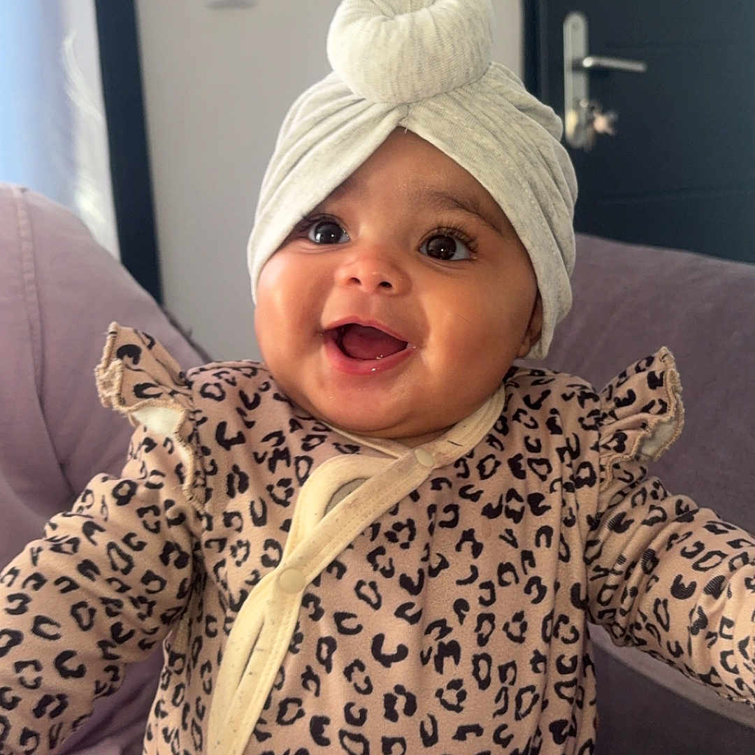 Syana participe au concours pour gagner de l'argent avec cette photo : baby, clothing, couch, curtain, cute, door, face, hand, happy, headwrap, indoor, infant, leopard_print, person, portrait, sitting, skin, smile, turban, young_child