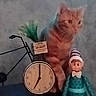 animal, background, bicycle, blurred, cat, clock, clock_face, decor, doll, feline, figurine, indoor, orange_tabby, ornament, pet, sitting, striped_hat, toy, vintage_style, whimsical