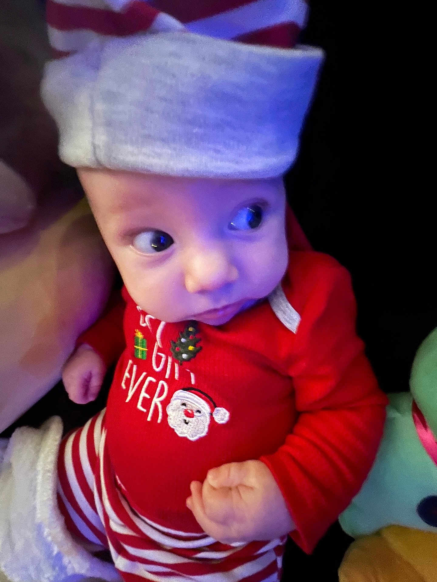 Vincent is registered to the contest to win money with this photo: baby, infant, child, pajamas, red_clothing, striped_pants, hat, holiday, christmas_theme, santa_face, cute, curious_look, indoors, close_up, hand, face, eyes, soft_lighting, cozy, festive
