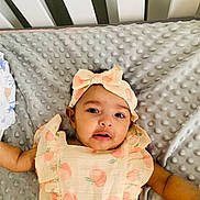Diya is registered to the contest to win money with this photo: baby, infant, child, headband, dress, peach_pattern, blanket, texture, bed, crib, cute, portrait, face, eyes, skin, arm, lying_down, indoor, soft, adorable