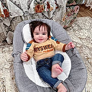 Miran is registered to the contest to win money with this photo: baby, child, infant, smiling, happy, portrait, indoors, high_chair, seated, casual_clothing, jeans, shirt, dark_hair, face, hand, feet, rug, chair, floral_pattern, home_decor