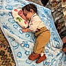 baby, sleeping, child, infant, portrait, blanket, pillow, blue_blanket, clothing, khaki_pants, brown_shoes, loafers, socks, indoors, bed, carpet, floral_bedding, strawberry, peaceful, cute