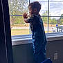 Cohen is registered to the contest to win money with this photo: child, toddler, overalls, denim, window, silhouette, profile, hands_on_glass, stool, socks, shoes, curtain, trees, car, street, outlet, indoor, daylight, curiosity, portrait