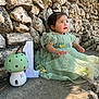 Delia is registered to the contest to win money with this photo: toddler, child, green_dress, stone_wall, butterfly, mushroom_decoration, number_one, outdoor, sunlight, celebration, sitting, curious, nature, portrait, cute, baby, flower_embroidery, grass, shadow, playful