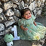 Delia is registered to the contest to win money with this photo: baby, child, girl, green_dress, floral_dress, smiling, happy, sitting, stone_wall, rocks, outdoor, sunlight, shadow, birthday, number_one, decorative_mushroom, cute, celebration, portrait, person