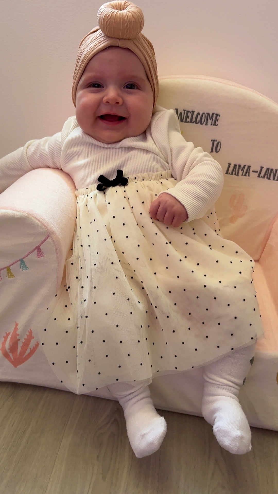 Aïtana a rejoint le concours — aidez-le/la à gagner de superbes lots ! baby, child, smile, happy, sitting, polka_dot, skirt, white_clothing, turban_hat, cushioned_chair, indoor, floor, wood_flooring, cute, portrait, infant, cozy, decor, text_on_chair, toddler