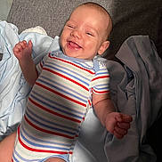 Houston is registered to the contest to win money with this photo: baby, bed, blanket, cheerful, child, comfort, cute, face, hand, happy, indoor, infant, lying_down, onesie, relaxing, skin, smiling, soft_lighting, striped_clothing, toddler