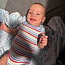 baby, bed, blanket, child, comfort, cute, fabric, face, hand, happy, head, indoors, infant, lying_down, onesie, portrait, skin, smiling, striped_clothing, young