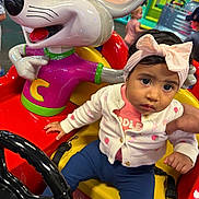 Ariana Castillo is registered to the contest to win money with this photo: amusement_center, baby, blue_pants, bow_headband, cardigan, cartoon_mouse, child, colorful, headband, indoor, infant, kiddie_ride, playground, portrait, sitting, steering_wheel, sweater, toy, vehicle, wide_eyed