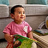 activity_table, baby, book, bracelet, child, colorful_book, cozy, curly_hair, earring, furniture, indoors, pink_shirt, playroom, portrait, reading, sitting, smiling, sofa, toddler, toy