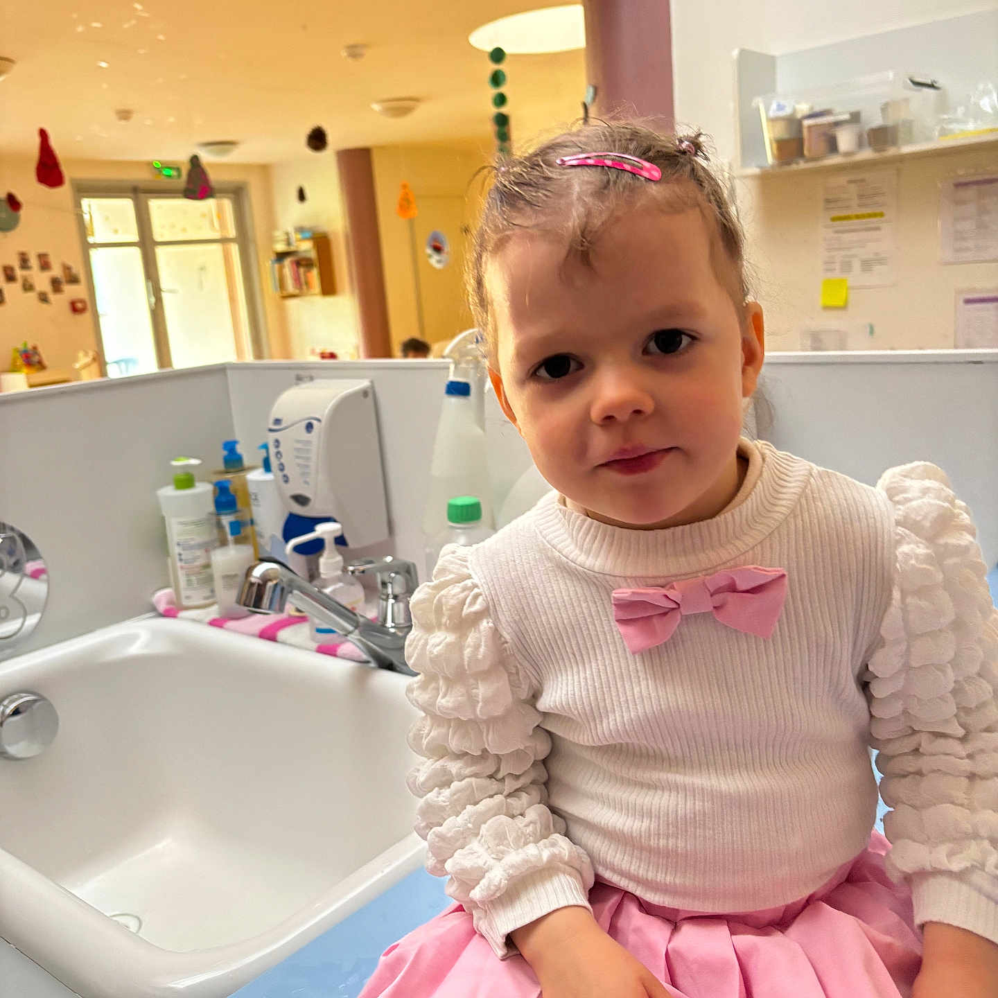 Julie participe au concours pour gagner de l'argent avec cette photo : bathroom, bottle, bow, child, cleaning_supplies, curly_hair, faucet, girl, hairclip, hand, indoor, lighting, pink_skirt, room, seated, sink, toddler, wall, white_sweater, window