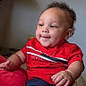 toddler, child, red_shirt, navy_shorts, indoor, cushion, smiling, curious, portrait, seated, baby, casual_clothing, short_hair, skin, happy, person, young_child, home, furniture, relaxed