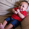 baby, child, infant, smiling, tongue_out, red_shirt, blue_shorts, leather_couch, sitting, happy, cute, portrait, indoor, casual, relaxed, playful, young_child, person, furniture, skin