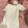 baby, infant, pacifier, hat, knitted_clothing, white_outfit, pink_blanket, lying_down, cute, newborn, sleepy, child, soft_texture, striped_hat, relaxing, small_hands, cozy, indoors, portrait, peaceful