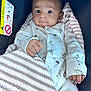 baby, infant, car_seat, blanket, onesie, dinosaur_pattern, striped_blanket, face, wide_eyes, curious, hand, clothing, seatbelt_warning, indoor, portrait, child, cute, soft_texture, newborn, cozy
