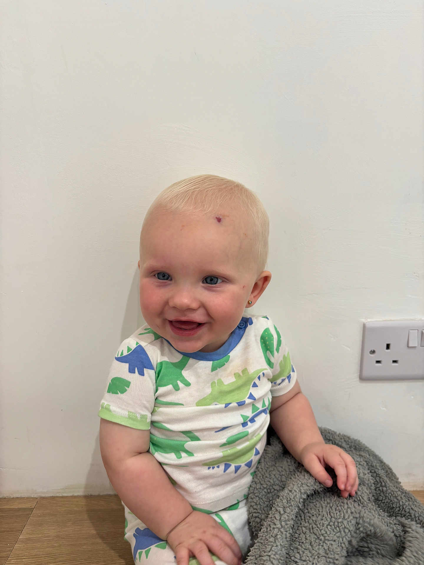 Marley joined the competition — help win amazing prizes! baby, child, smiling, sitting, indoor, dinosaur_pattern, blue_eyes, short_hair, white_wall, wooden_floor, blanket, cute, happy, earrings, casual_clothing, power_outlet, infant, portrait, playful, toddler