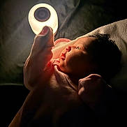 Jurnee is registered to the contest to win money with this photo: baby, infant, hand, light, glow, darkness, curious, face, portrait, newborn, soft_light, expression, candle_like, indoor, blanket, clothing, skin, person, closeup, warm_light
