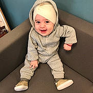 Kim a rejoint le concours — aidez-le/la à gagner de superbes lots ! baby, child, smiling, hoodie, headwrap, sitting, chair, footwear, grey_clothing, indoor, happy, cute, portrait, young_child, person, shoes, cozy, casual_wear, infant, small_hands