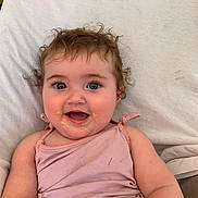 Mélyna a rejoint le concours — aidez-le/la à gagner de superbes lots ! baby, child, curly_hair, cute, expression, eyes, face, food_stains, happy, indoor, infant, messy, mouth, person, pillow, pink_clothing, portrait, skin, smile, tank_top
