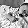 baby, infant, smile, knitted_blanket, face, hand, card, text, black_and_white, happy, lying_down, young_child, portrait, cozy, indoors, cute, head, clothing, skin, closeup