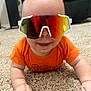 Nathaniel is registered to the contest to win money with this photo: baby, infant, crawling, orange_onesie, sunglasses, carpet, indoor, smiling, cute, child, reflection, face, hand, skin, head, person, playful, young, happy, clothing
