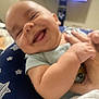 Nathaniel is registered to the contest to win money with this photo: baby, smiling, closeup, face, infant, hands, cushion, star_pattern, home, television, blurred_background, happy, child, person, blue, clothing, skin, cute, portrait, playful
