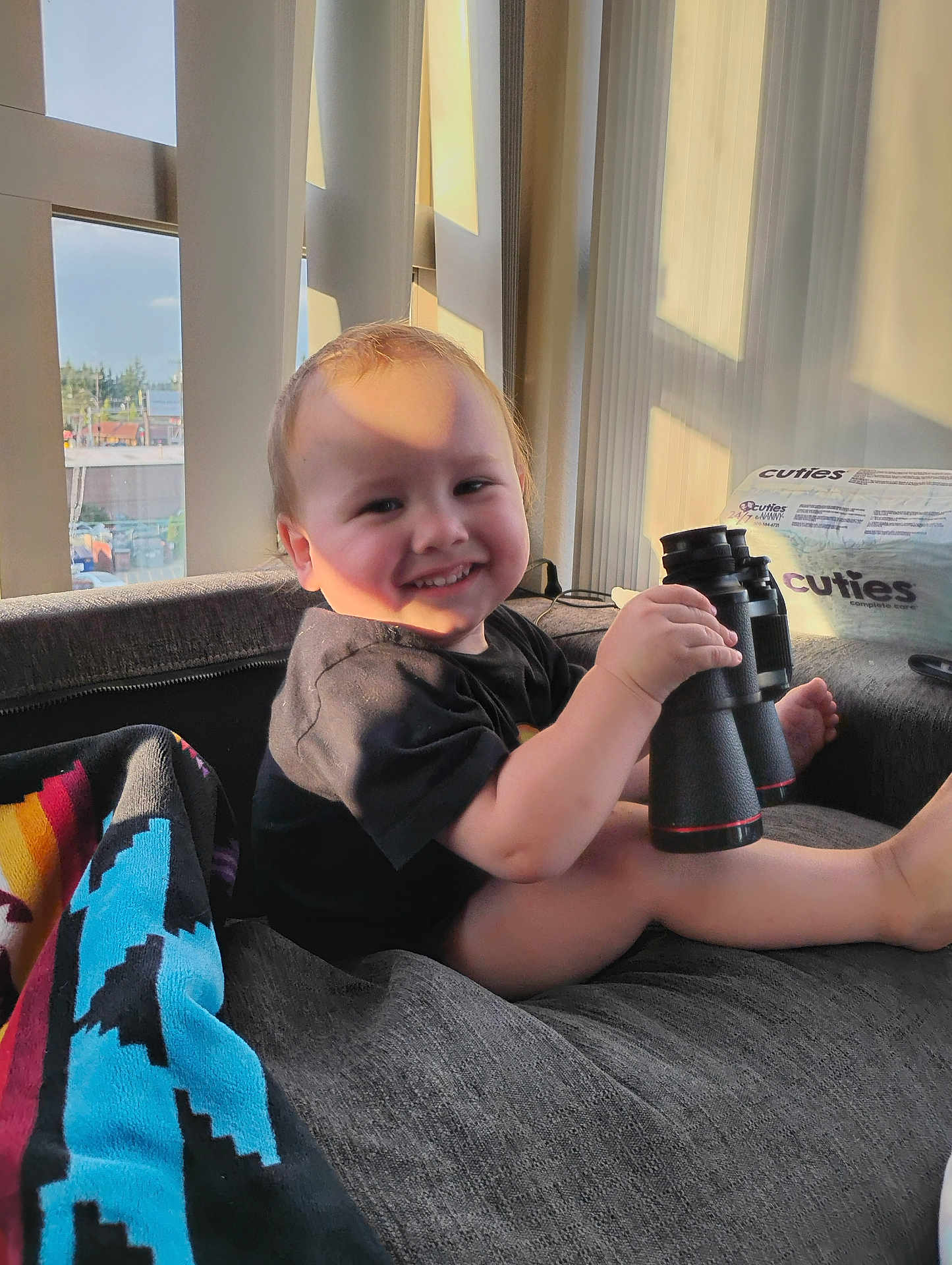 Ezekiel is registered to the contest to win money with this photo: toddler, child, binoculars, smile, indoor, couch, blanket, window, sunlight, shadow, curtains, clothing, toy, home, relaxing, person, furniture, happy, face, legs