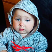 Ezekiel is registered to the contest to win money with this photo: toddler, child, hoodie, clothing, indoor, face, blue_eyes, expression, person, sitting, furniture, drawer, hood, red_logo, casual, portrait, young_child, cute, soft_lighting, closeup