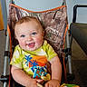baby, child, smiling, blue_eyes, stroller, camo_pattern, tie_dye_shirt, indoor, carpet, toy, blanket, happy, person, infant, clothing, seat, hand, face, cute, portrait
