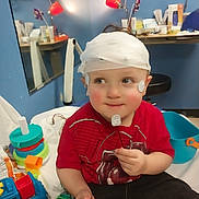 Charles is registered to the contest to win money with this photo: child, toddler, bandage, medical_sensor, red_shirt, toys, colorful_toys, hospital_room, blue_wall, mirror, table, lamp, stool, medical_equipment, playful, cute, indoor, smiling, face, person