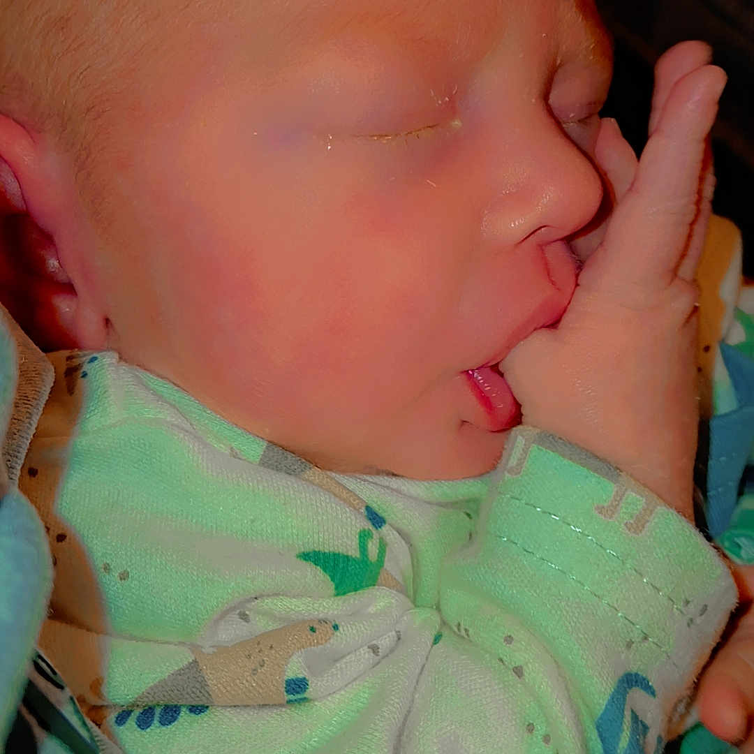 Cashton is registered to the contest to win money with this photo: baby, blanket, child, closeup, comfortable, cute, dinosaur_pattern, face, hand, indoors, infant, newborn, onesie, peaceful, portrait, rest, skin, sleeping, thumb_sucking, young