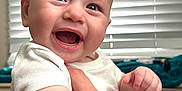 Ethan is registered to the contest to win money with this photo: baby, smiling, infant, happy, face, hand, adult_hand, indoor, window_blinds, lamp, white_clothing, closeup, portrait, cute, human, skin, expression, joy, child, holding