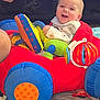 Holden is registered to the contest to win money with this photo: baby, child, toy, plush_toy, car_toy, smiling, happy, indoor, person, colorful, red, blue, green, yellow, face, infant, play, joy, cushion, adult