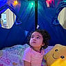 Sypha is registered to the contest to win money with this photo: toddler, child, tent, indoor, plush_toy, star_plush, string_lights, colorful_lights, curly_hair, pink_clothing, blanket, cozy, looking_up, playtime, soft_toy, cute, home, curious, young_child, smiling_toy