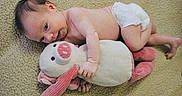Freya joined the competition — help win amazing prizes! baby, infant, diaper, plush_toy, stuffed_animal, carpet, indoor, child, cute, soft_texture, pink, white, relaxed, lying_down, young_child, toy, toddler, person, cuddling, floor