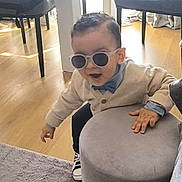 Ayssem participe au concours pour gagner de l'argent avec cette photo : toddler, child, sunglasses, bow_tie, cardigan, indoor, ottoman, wooden_floor, rug, chair, hand, motion, casual_clothing, cute, fun, person, furniture, shoes, light, playful