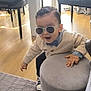 toddler, child, sunglasses, bow_tie, cardigan, indoor, ottoman, wooden_floor, rug, chair, hand, motion, casual_clothing, cute, fun, person, furniture, shoes, light, playful
