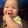 toddler, child, smiling, curly_hair, hand, shirt, cartoon_graphic, indoor, face, happy, person, baby, fingers, cute, portrait, closeup, seated, skin, cheeks, dimple