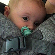 Phoebe is registered to the contest to win money with this photo: baby, pacifier, baby_carrier, pink_pajamas, polka_dots, face, close_up, person, infant, adult, skin, comfort, holding, strap, fabric, head, eyes, mouth, indoor, parent