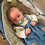 baby, infant, pacifier, baby_carrier, blue_dress, floral_pattern, long_sleeve_shirt, cozy, padded, indoor, child, cute, comfort, person, newborn, clothing, face, head, hand, relaxing