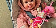Phoebe joined the competition — help win amazing prizes! baby, child, stroller, pink_jacket, plush_toy, caterpillar_toy, cute, smiling, tongue_out, infant, outdoor, warm_clothing, seatbelt, person, face, playful, toy, fabric, colorful, happy