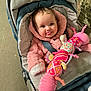 baby, child, stroller, pink_jacket, plush_toy, caterpillar_toy, cute, smiling, tongue_out, infant, outdoor, warm_clothing, seatbelt, person, face, playful, toy, fabric, colorful, happy