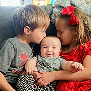 Lennox is registered to the contest to win money with this photo: baby, boy, girl, child, couch, cuddle, kiss, smile, happy, indoor, family, love, affection, clothing, red_dress, grey_shirt, patterned_pants, hair_bow, portrait, toddler