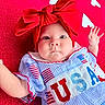 baby, infant, red_bow, headband, usa, american_flag, dress, blanket, heart_pattern, cute, child, portrait, lying_down, hand_raised, clothing, blue, red, white, adorable, expression