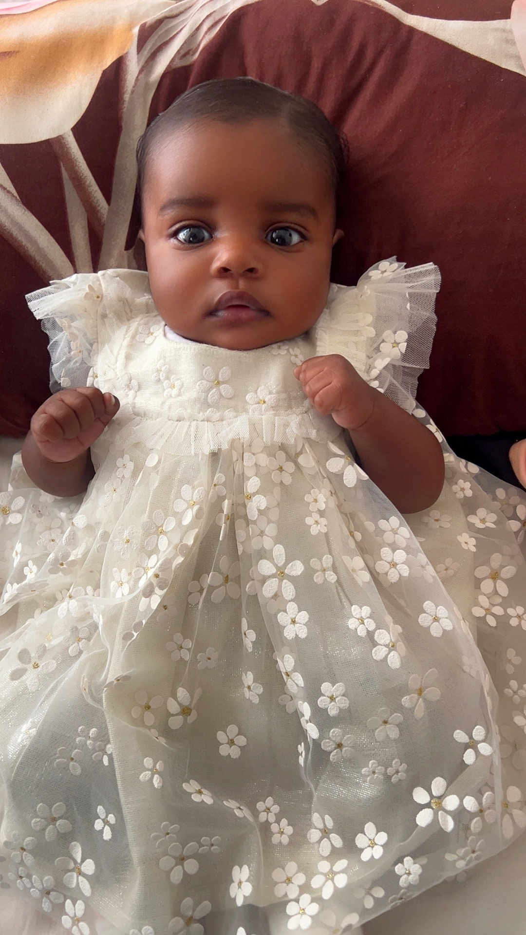 Miracle is registered to the contest to win money with this photo: adorable, baby, child, closeup, cushion, cute, dress, eyes, fabric, face, floral_pattern, hands, indoor, infant, pillow, portrait, soft_lighting, texture, white_dress, young